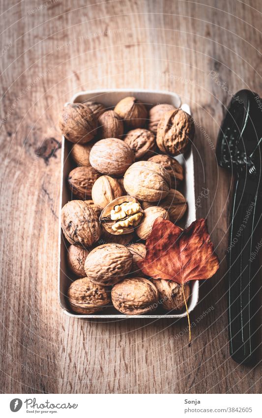 Whole walnuts in a bowl and a nutcracker on a brown wooden table. Walnut Nutcrackers Rustic Autumn leaves Autumnal Close-up Protein Leaf Brown shell Delicious