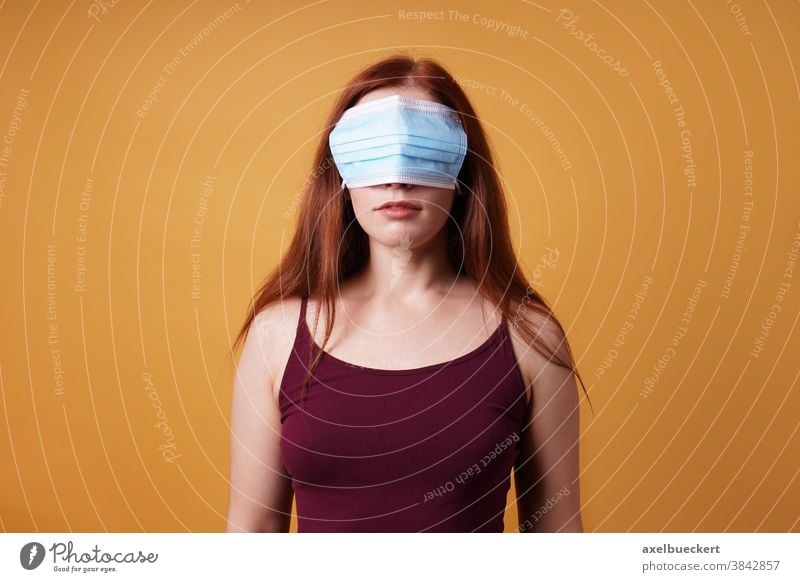 young woman wearing medical face mask over her eyes - corona denier cover covid coronavirus denial deny blind wrong protest covid-19 people adult person