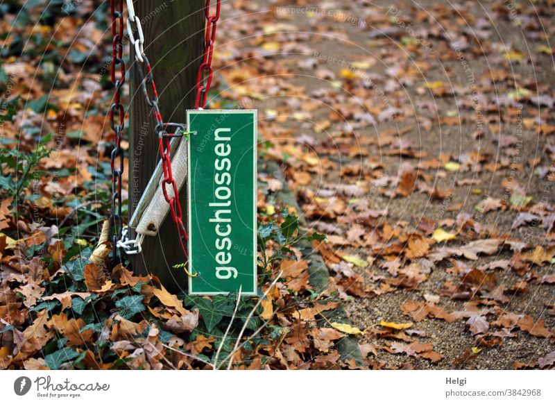 open - sign "closed" hangs together with a chain on a pole next to the path, which is covered with autumn leaves Closed cordon Shut-off chain stake foliage