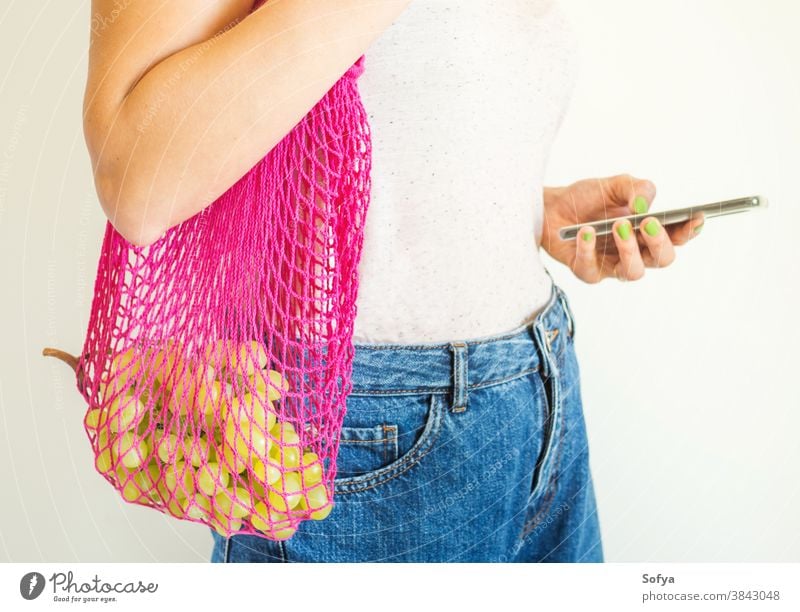 Young woman with reusable mesh bag and smartphone food using mobile phone online delivery grocery fruit grapes autumn plastic sustainable digital zero waste