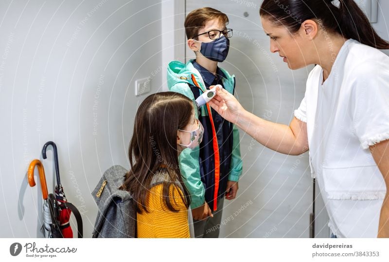 Mother checking her daughter's temperature before going to school mother thermometer fever coronavirus before going school protective mask home family indoors