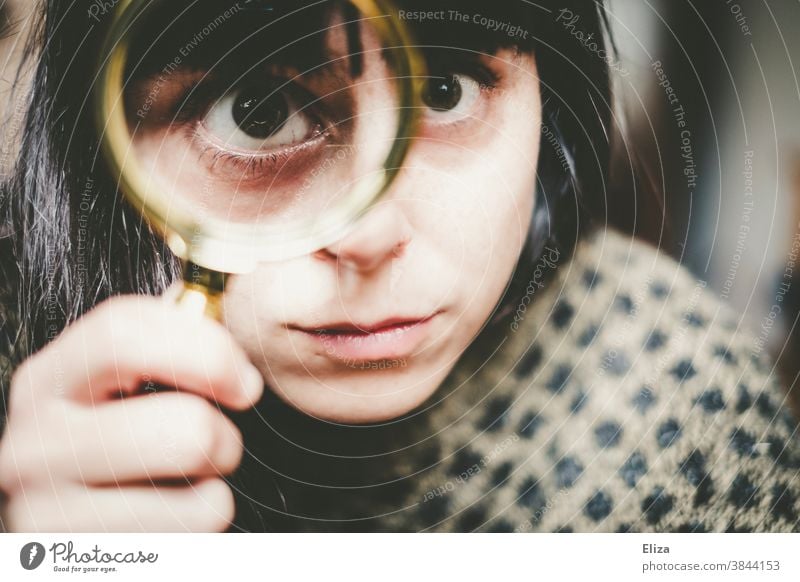 Young woman looks more closely through a magnifying glass. Magnifying glass Enlarged Eyes Investigate test see Squint warped Face search Lens Looking Detective