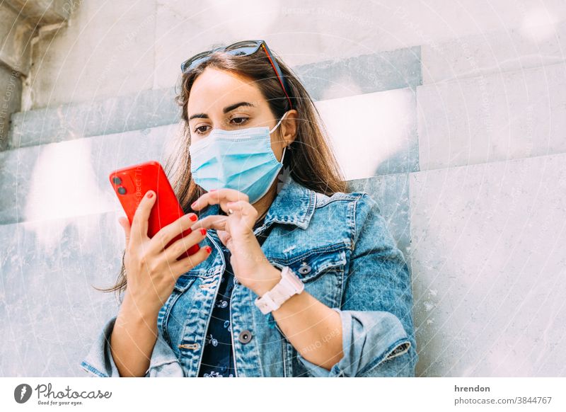 woman with a face mask leaning against the wall using her smartphone female young lifestyle internet communication technology mobile telephone communicate