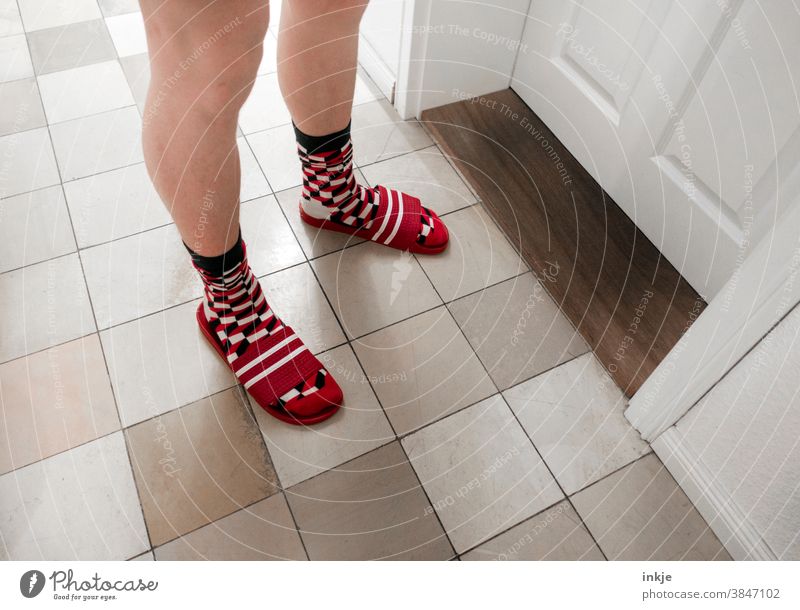 Pale legs stand before a closed door. Checked socks in striped flip-flops. Colour photo Interior shot Legs Boy (child) young man Stand Day Room Hallway