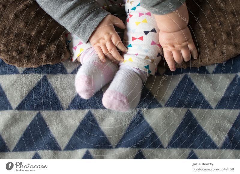 Baby reaching for feet, dimpled baby hands, triangle print blanket and pants child foot newborn love small toes care human kid childhood little family barefoot