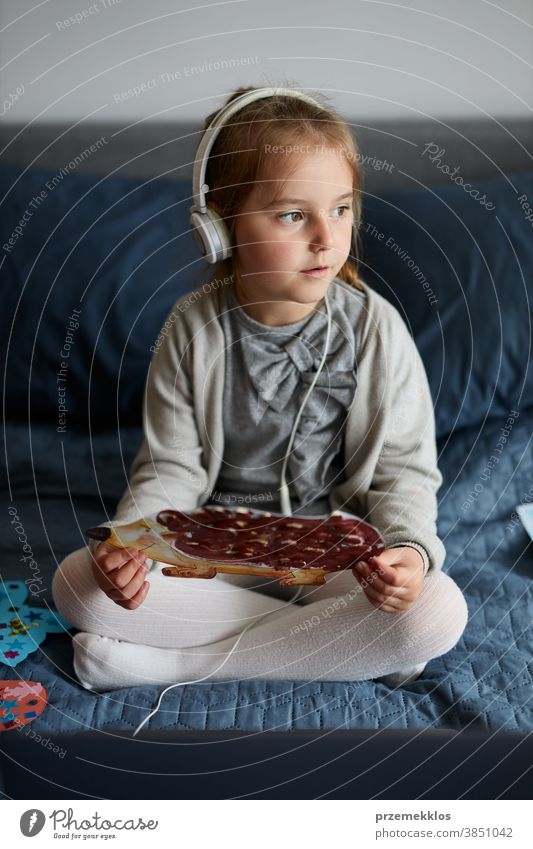 Little girl preschooler learning online showing her works drawings done at home child watching listening educational puzzle bed internet small room game movie