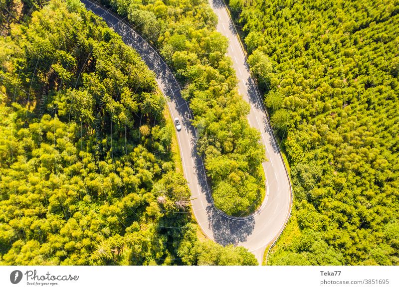 an forest street curve with a speeding car from above curvy street forest from above street from above green white white cabrio trees