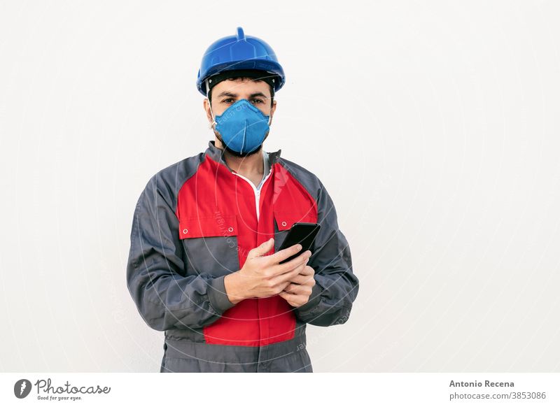 Bearded worker man with face mask looking smart phone covid-19 uniform security pandemic virus white background wall coronavirus surgical mask protection