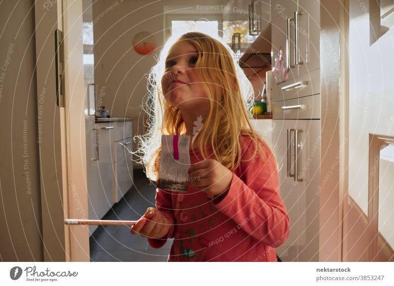 Small Caucasian Girl Holding Sign and Pencil in Home Kitchen child girl play blond caucasian lifestyle female indoor natural lighting grow learn pencil write