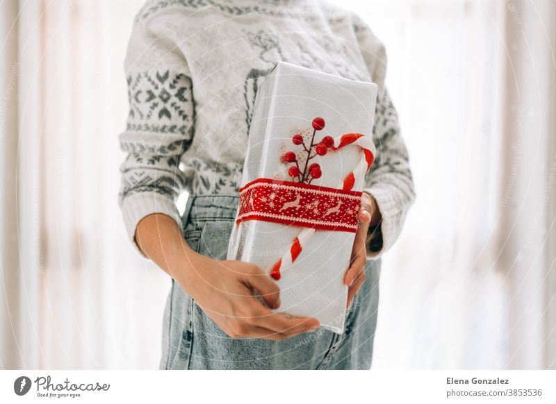 Young unrecognizable woman holds in a gift box in metallic paper with red twine and candy. Christmas New Years present. christmas merry christmas new year