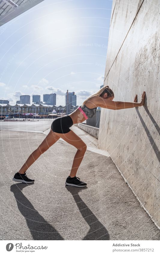 Sportswoman stretching legs near wall of building sportswoman lean exercise warm up active training city female athlete fitness sportswear healthy body young