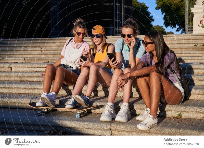 Group of teenagers with smartphones sitting on steps in city girlfriend urban together cheerful using trendy mobile women young multiracial multiethnic diverse