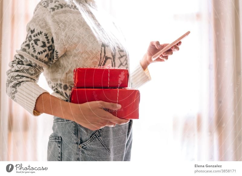 Young unrecognizable watching her mobile phone woman watching her mobile phone holds red gift boxes. Christmas New Years present. christmas merry christmas