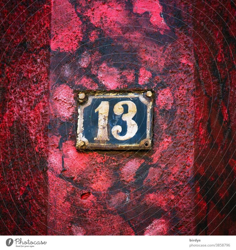 Weathered house number 13 on red - black house wall. Number 13 House number Old Rust Red Black Colour Superstition Digits and numbers Central perspective
