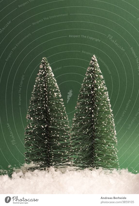 Two fir trees with snow on a green paper background, space for text on top creative traditional snowflake minimal trendy greeting copy space template