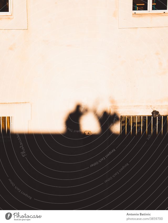 Outlines, sihouettes as shadows are cast on a stone house of two people standing together. One person taking the photo while the other one holds their hands in the air