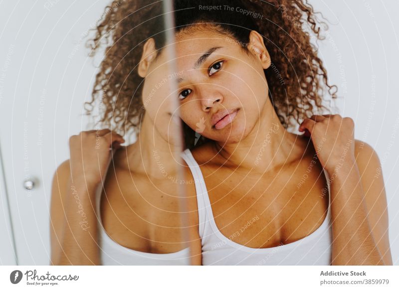 Relaxed ethnic woman with curly hair standing near mirror at home calm relax afro morning reflection casual young female african american black hairstyle
