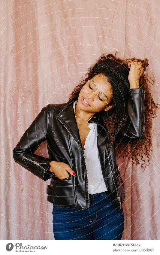 Stylish black woman in leather jacket in studio style afro hairstyle trendy casual touch hair young carefree female ethnic african american outfit cool modern