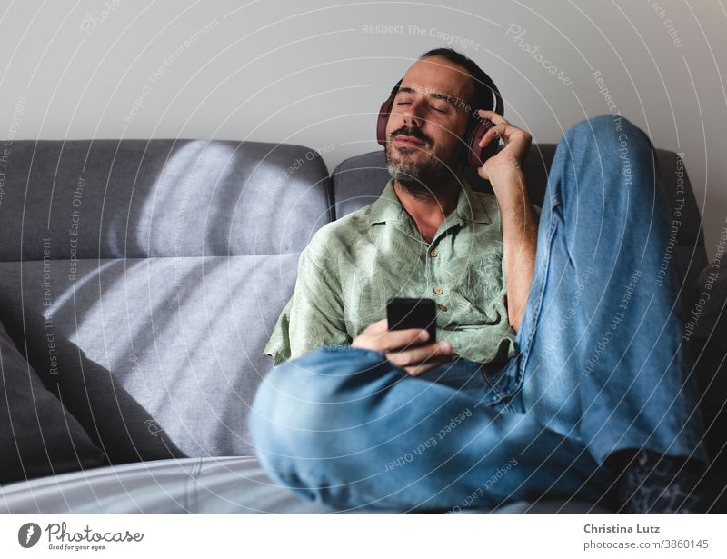 Man sitting on sofa in the living room listening to music with headphones man relax home people mobile person communication telephone smiling white technology
