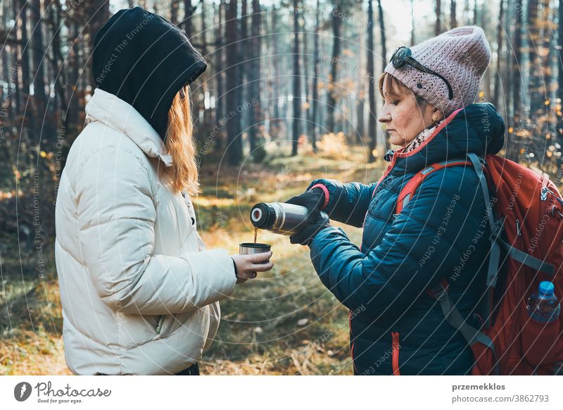 Mother and daughter with backpack having break during autumn trip on autumn cold day active activity adventure backpacker coffee cup destination drink enjoy