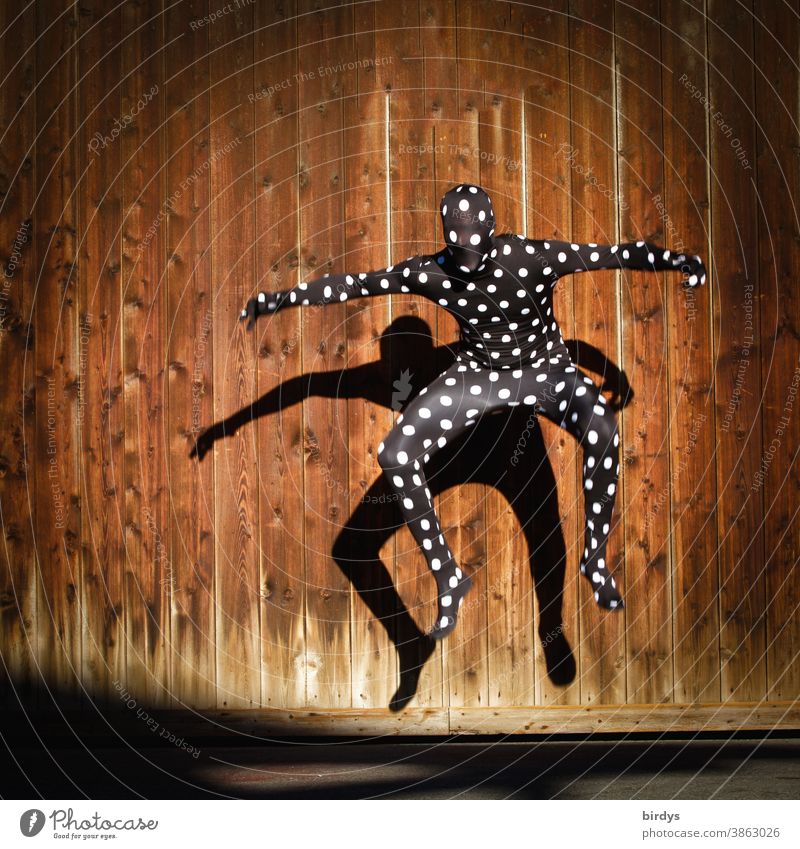 Human figure in dotted morphsuit costume, jumping into the air with shadow cast on a wooden wall Human being Morph Suite full body suit points in a dive