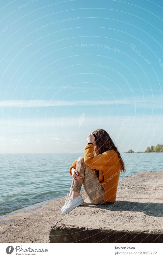 Female sitting on a stone stairs on a beach hugging her knees female sea relax lifestyle person leisure ocean water outdoors sweater autumn nature sky landscape