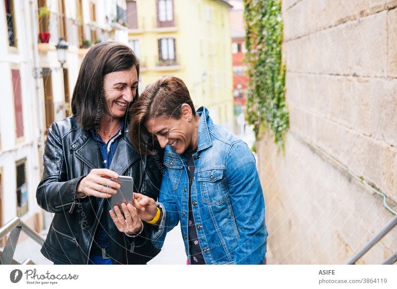 Funny middle aged lesbian couple laughing at something in the mobile phone LGBTQ gay 40 50 selfie smartphone self portrait smile homosexual women real people