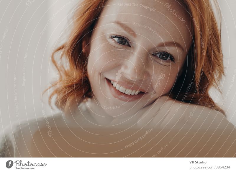 Close up shot of positive redhead woman with freckled skin and toothy smile, concentrated at display of laptop computer, satisfied with online business, checks received message, has remote job