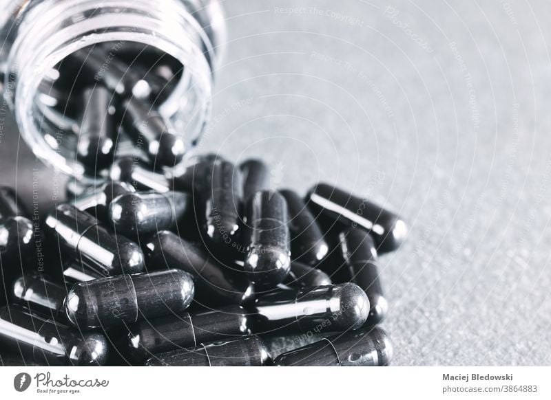 Close up picture of black capsules spill out of container. drug medicine poison addiction danger death treatment medical pharmacy healthy therapy science
