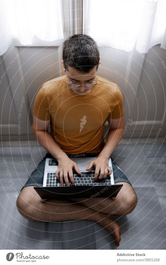 Busy man working on laptop in living room freelance remote home typing project concentrate browsing male casual outfit floor sit window legs crossed device job