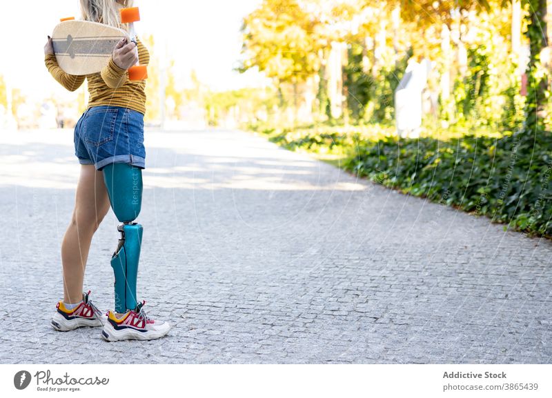 Front view of smiling female with bionic leg prosthesis sitting in street  and enjoying music in headphones on sunny day stock photo - OFFSET