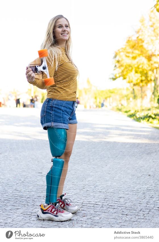 Slim woman with longboard and leg prosthesis on street bionic skater artificial limb disable urban female skateboard town modern sunlight sunny amputee summer