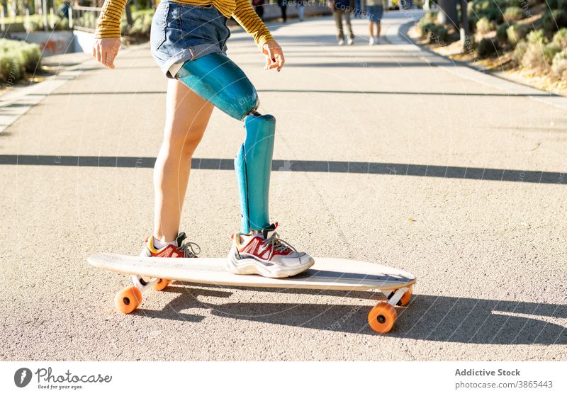 Crop woman riding longboard in city bionic prosthesis ride skater leg cheerful disable artificial limb female amputee street urban optimist town skateboard