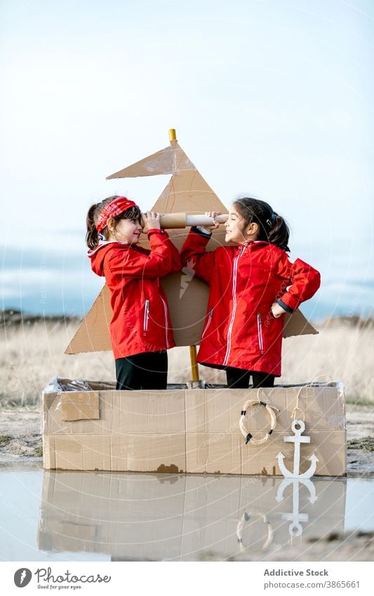 Girls playing in carton boat in puddle cardboard child together having fun imagination game girl spyglass handmade cheerful happy enjoy smile kid childhood