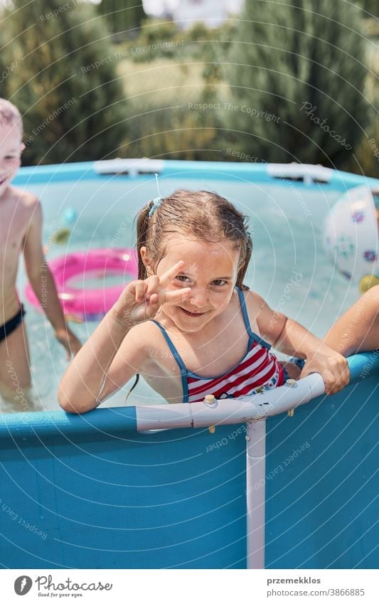 Happy girl making V sign gesture playing in a pool enjoying splashing having fun with siblings on a summer sunny day authentic backyard childhood children