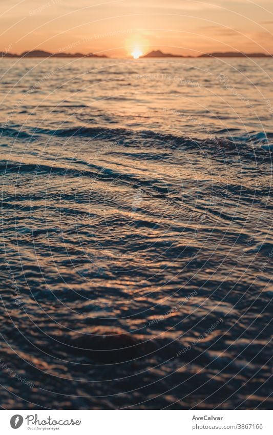 Vertical image of a tide on the beach over the sand during a colorful sunset with the islands as the background and copy space ocean wave sunrise gold surf