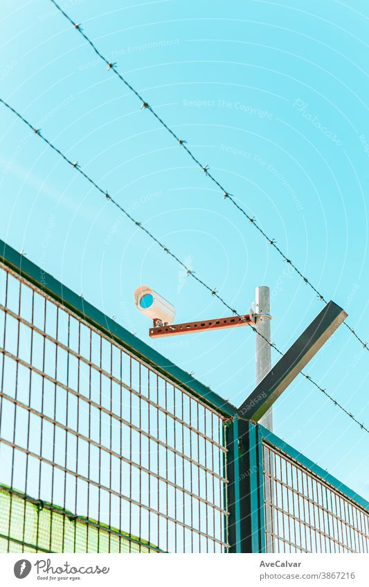 Minimalistic and colorful shot of a surveillance camera with a wall and a barbed wire private protection safety system guard lens security video cctv control