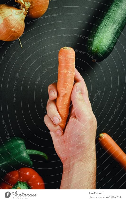 Hand grabbing a carrot surrounded by vegetables with a black table culinary kitchen cuisine cooking chopping board preparation knife cutting board food wooden