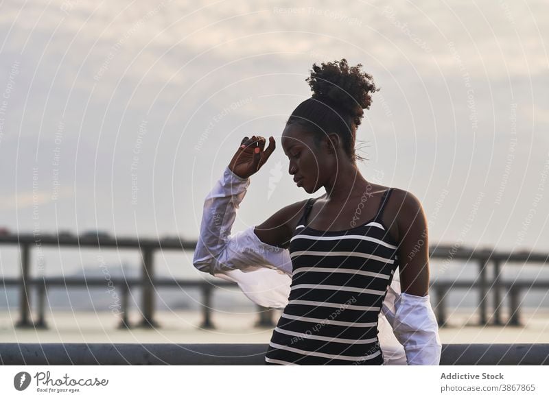 Calm black woman standing on city embankment at sunset sea tranquil pensive relax calm sunlight urban young female african american ethnic seafront thoughtful