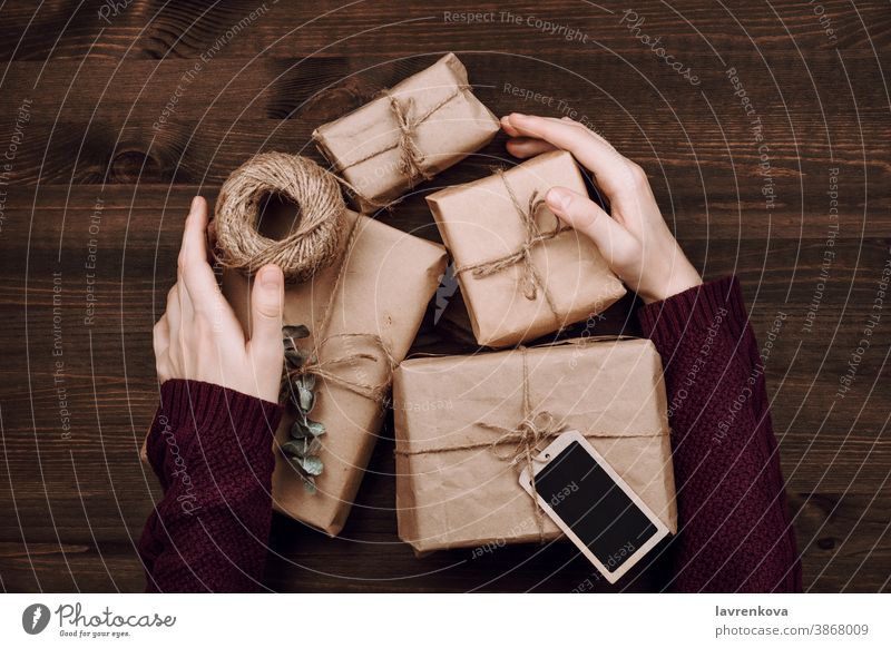 woman's hands in sweater holding wrapped presents and roll of string on wooden background sustainable beautiful birthday box celebration christmas craft
