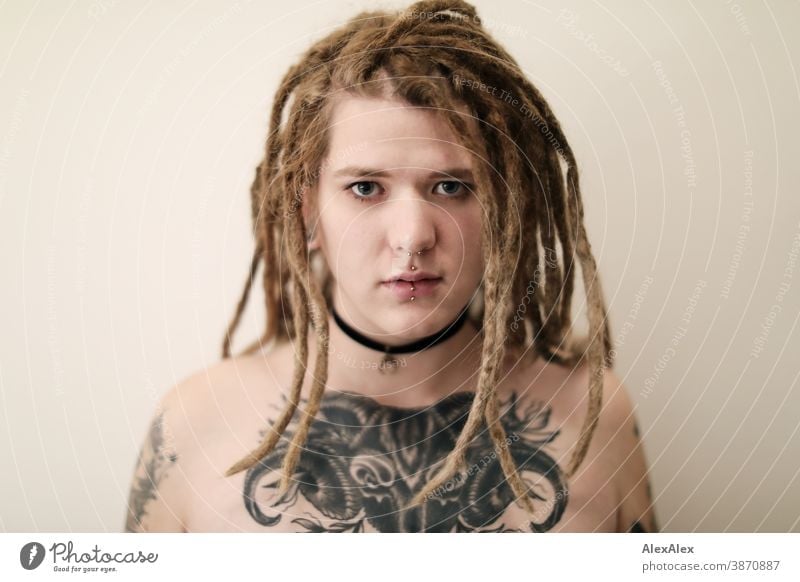 Portrait of a young woman with dreadlocks, who has a large tattoo of an ox head on her décolleté Woman Dirty Blonde tattooing Jewellery Piercing earring Chest