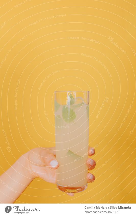 Young woman hand holding a glass of cocktail with mint. Studio photo with yellow background. alcohol beverage celebration citrus closeup copy space drink fresh