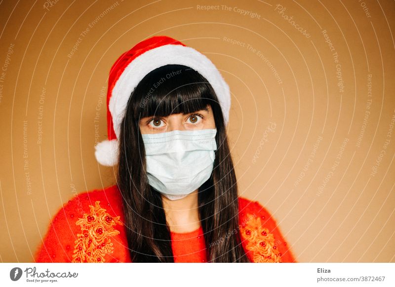 Young woman in christmassy clothes is wearing a mouth guard and a Santa cap. Christmas during the Corona Pandemic. Mask Disposable mask Christmas mood