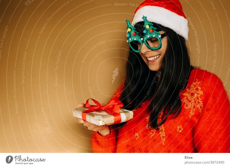 Young woman in christmassy clothes looks smiling at a christmas present Christmas Woman Christmas gift garments Sweater Red Gift Giving of gifts Donate get Joy
