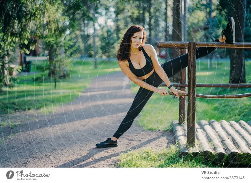 Brunette woman in black leggings, top and sneakers is posing