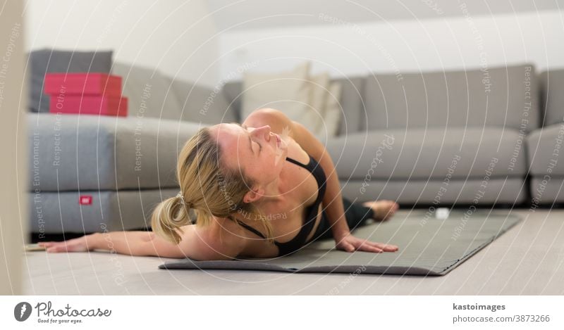 Beautiful blonde woman doing home workout indoors. Woman practice yoga at home. Fit girl using workout tutorials for healthy active lifestyle. Woman using quarantine for home workouts.