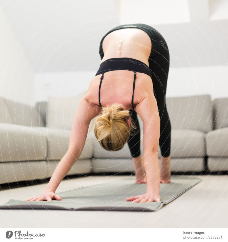 Beautiful blonde woman doing home workout indoors. Woman practice yoga at  home. Fit girl using workout tutorials for healthy active lifestyle. Woman  using quarantine for home workouts. - a Royalty Free Stock