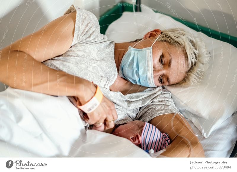 A new mother nursing her newborn boy in mask during pandemic baby delivery hospital breast feeding ward clinic patient small happy little mom nurse first corona