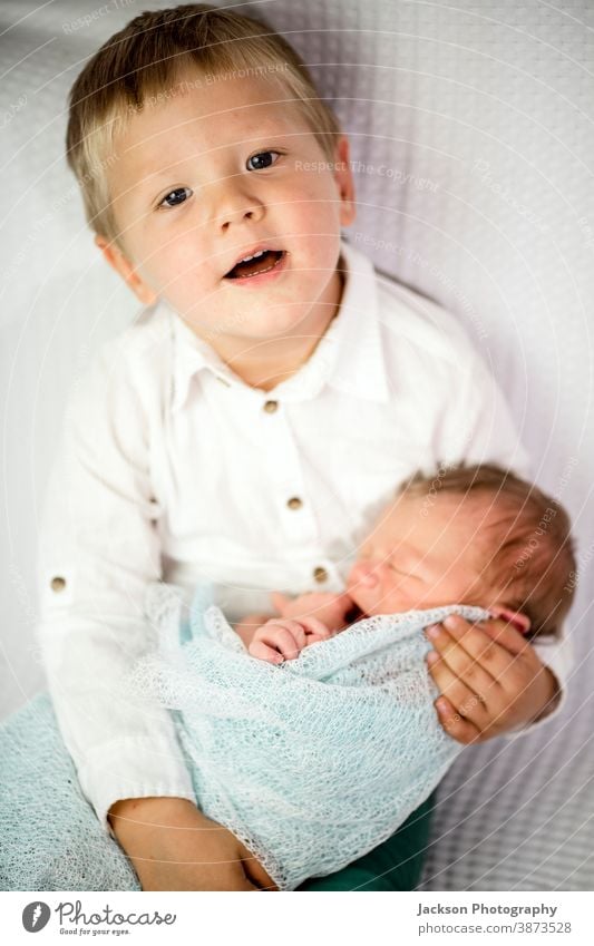 Three year old boy holds his newborn brother Brothers and sisters Family Love Sibling Wrap Caucasian Blonde Face Appearance Smiling hug care Emotions