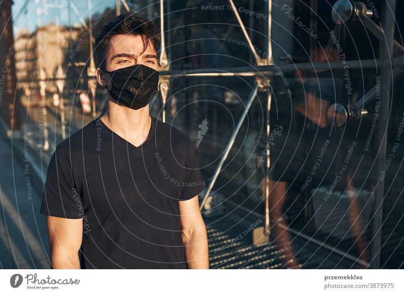 Young man walking in the city center along glass store front wearing the face mask to avoid virus infection boy care caucasian contagious conversation corona